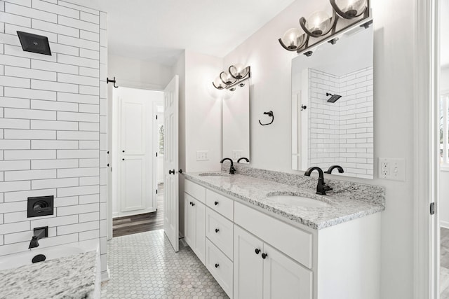 bathroom with double vanity, tile patterned flooring, a tile shower, and a sink