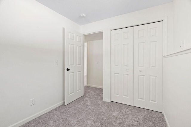 unfurnished bedroom with a closet, light carpet, and baseboards