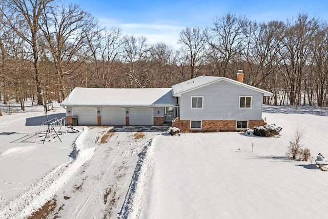 snow covered property with a garage, brick siding, and a chimney