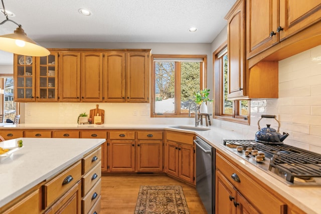 kitchen featuring brown cabinetry, glass insert cabinets, stainless steel appliances, light countertops, and a sink