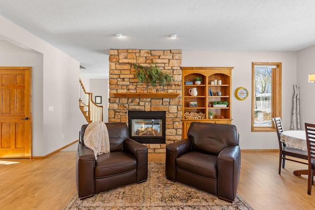 living area with stairway, light wood-type flooring, a stone fireplace, and baseboards