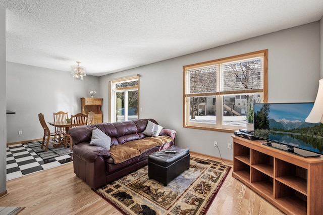 living area featuring light wood finished floors, a textured ceiling, baseboards, and a notable chandelier