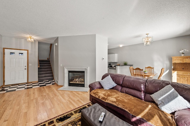 living area featuring light wood finished floors, a glass covered fireplace, stairs, a textured ceiling, and a chandelier