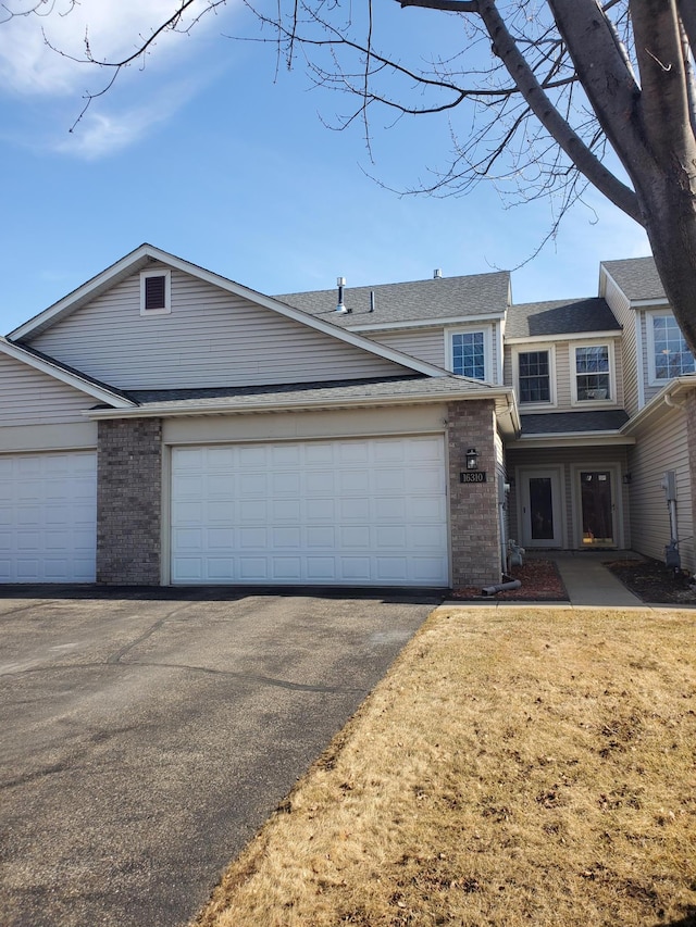 view of front facade featuring a garage, driveway, a shingled roof, and brick siding