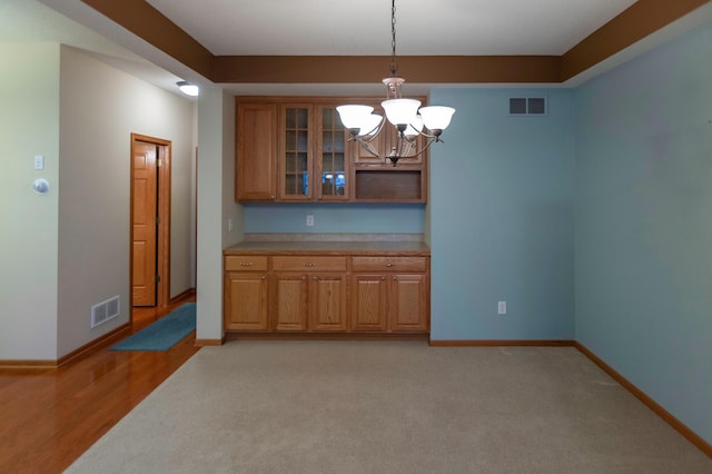 unfurnished dining area featuring light colored carpet, visible vents, baseboards, and an inviting chandelier