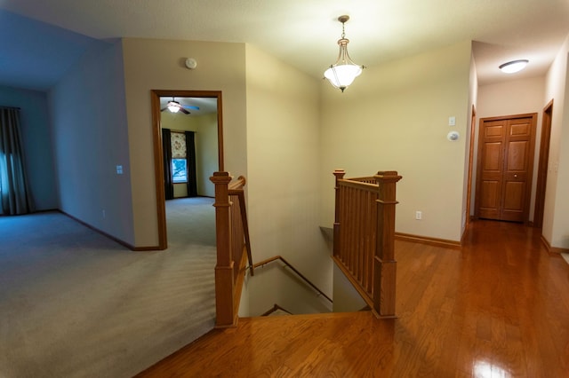 corridor with carpet, baseboards, an upstairs landing, and wood finished floors