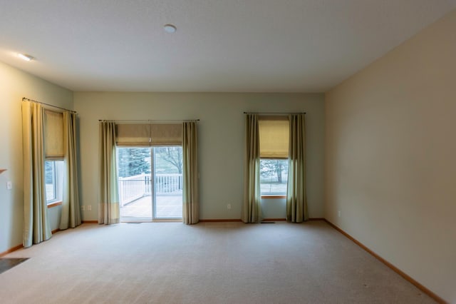 spare room featuring light colored carpet and baseboards