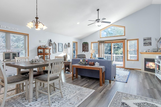 dining area featuring high vaulted ceiling, ceiling fan with notable chandelier, a tiled fireplace, and wood finished floors