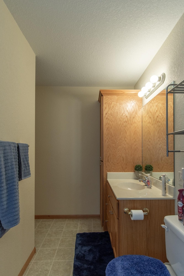 bathroom featuring a textured ceiling, tile patterned flooring, toilet, vanity, and baseboards