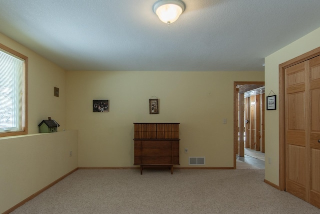 unfurnished room with light colored carpet, visible vents, a textured ceiling, and baseboards