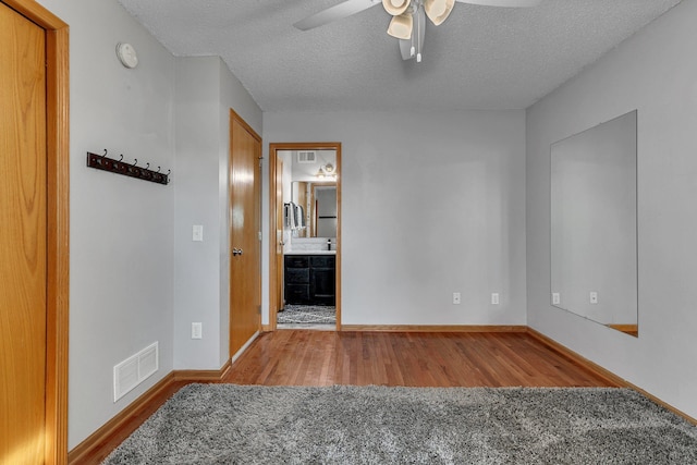 empty room featuring visible vents, a ceiling fan, a textured ceiling, wood finished floors, and baseboards