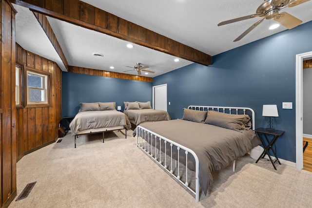 bedroom with ceiling fan, a textured ceiling, light colored carpet, beamed ceiling, and wood walls