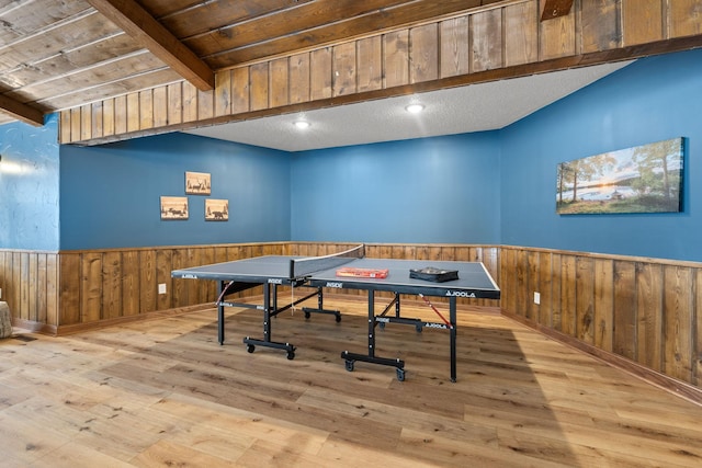 recreation room with wood walls, hardwood / wood-style flooring, wainscoting, and beam ceiling