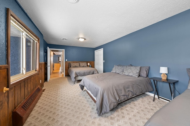 bedroom featuring carpet, a wainscoted wall, radiator, wooden walls, and a textured ceiling