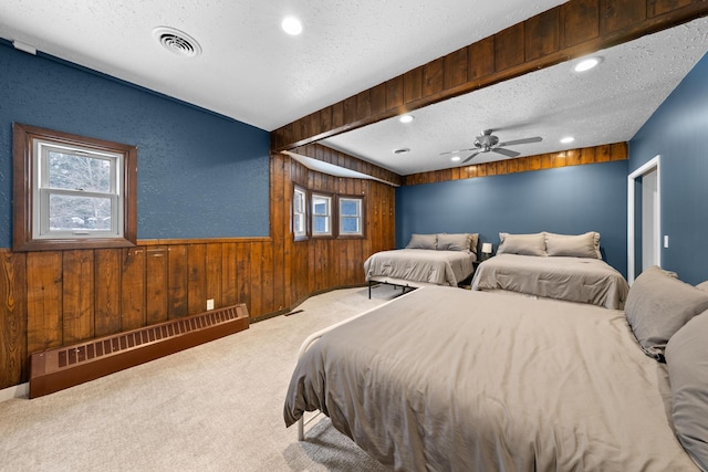 bedroom featuring carpet floors, visible vents, baseboard heating, wooden walls, and a textured ceiling