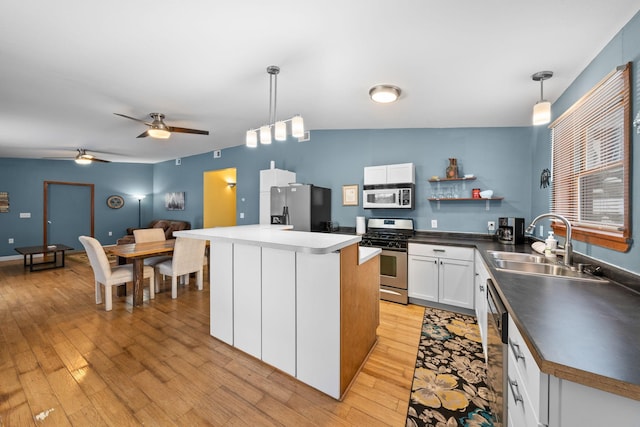 kitchen with stainless steel appliances, a sink, white cabinetry, light wood-type flooring, and pendant lighting