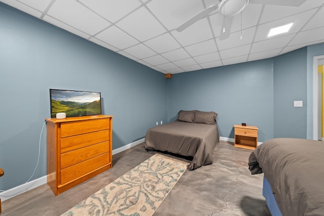 bedroom featuring concrete flooring, a drop ceiling, and baseboards