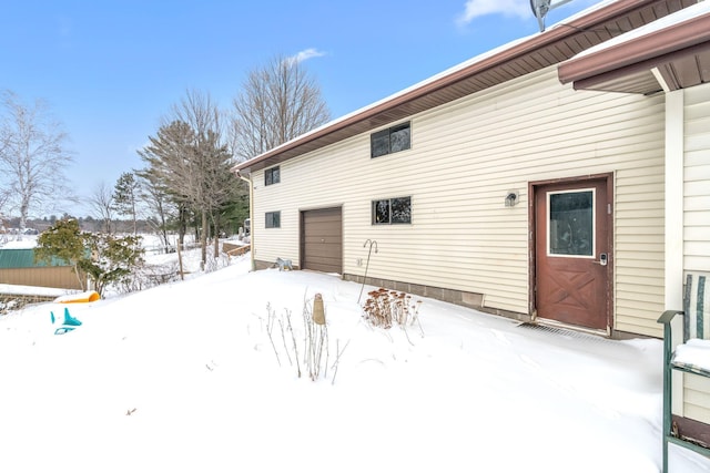 snow covered rear of property featuring a garage