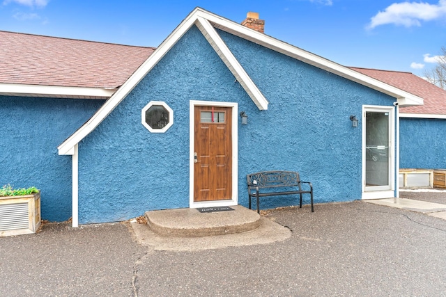 exterior space with roof with shingles, a patio, a chimney, and stucco siding