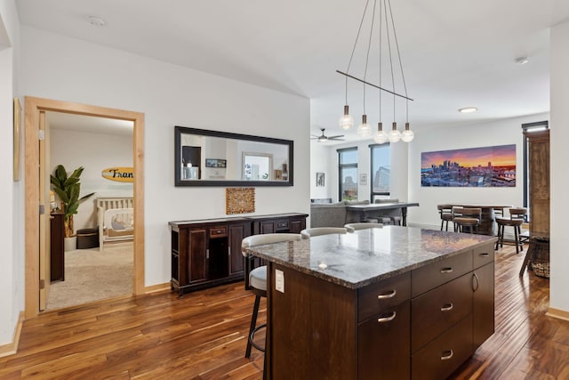1240 2nd St Unit 704, Minneapolis, MN 55415 - kitchen featuring a kitchen breakfast bar, dark brown cabinets, dark wood-style floors, hanging light fixtures, and dark stone countertops