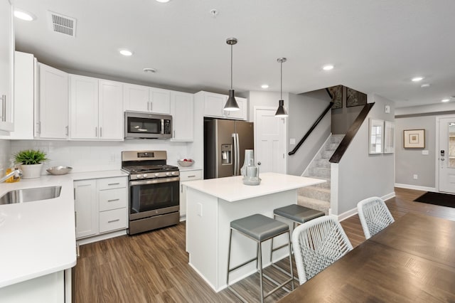 kitchen with decorative light fixtures, a center island, appliances with stainless steel finishes, dark hardwood / wood-style floors, and white cabinets