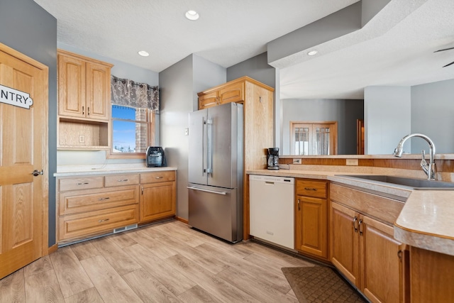 kitchen featuring high end fridge, light countertops, white dishwasher, a sink, and light wood-type flooring