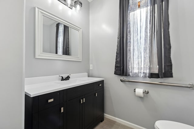 half bathroom featuring toilet, vanity, and baseboards