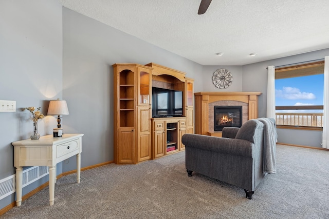 living room with light carpet, a glass covered fireplace, a textured ceiling, and baseboards