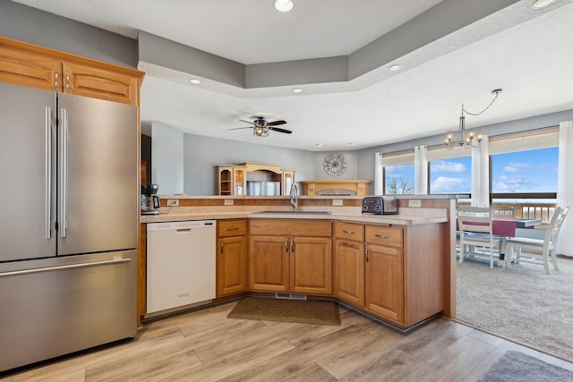 kitchen with light countertops, ceiling fan with notable chandelier, freestanding refrigerator, white dishwasher, and a sink