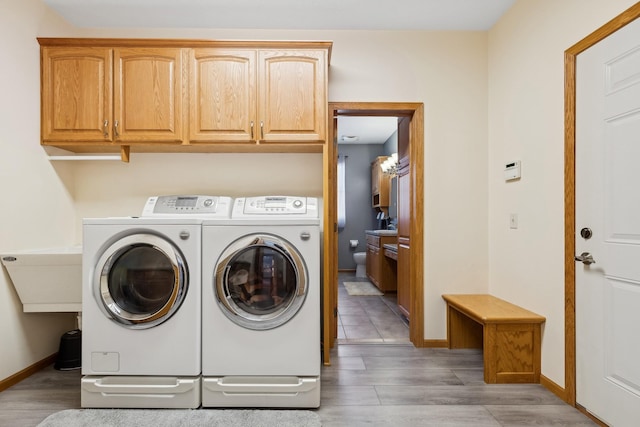 laundry room with cabinet space, washing machine and dryer, light wood-style flooring, and baseboards