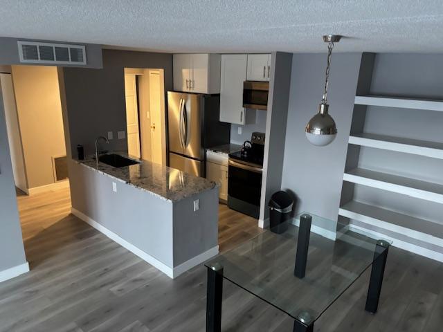 kitchen with appliances with stainless steel finishes, pendant lighting, sink, white cabinets, and dark stone counters