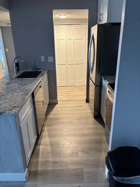 kitchen with sink, appliances with stainless steel finishes, light stone countertops, light hardwood / wood-style floors, and white cabinets