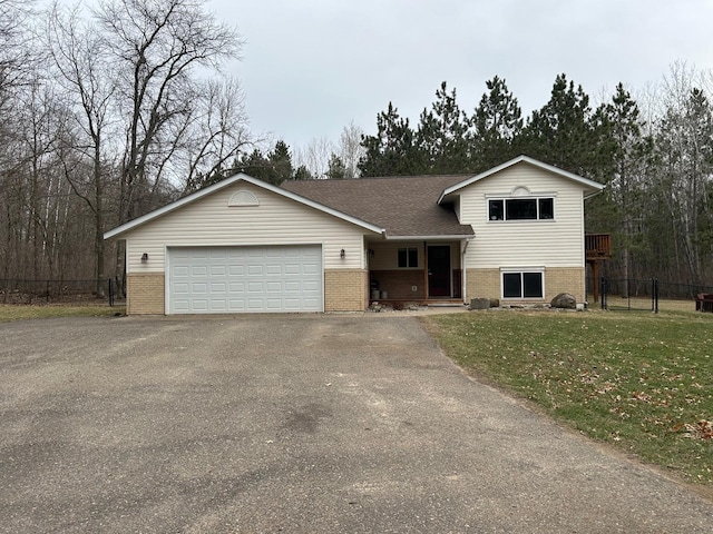 split level home with fence, driveway, brick siding, a front yard, and a garage