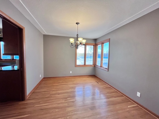 unfurnished dining area with a textured ceiling, a notable chandelier, and light hardwood / wood-style flooring