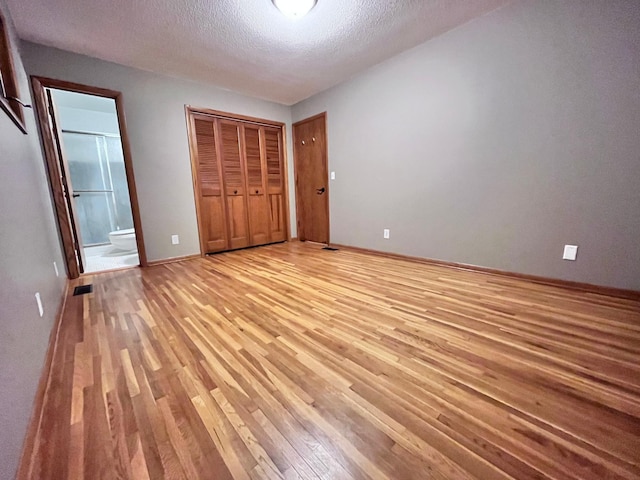 unfurnished bedroom featuring light wood-type flooring, a closet, ensuite bathroom, and a textured ceiling