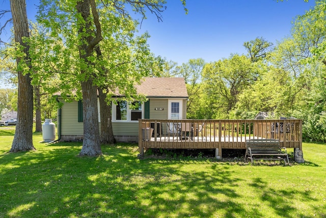 back of property featuring a wooden deck, a yard, and roof with shingles