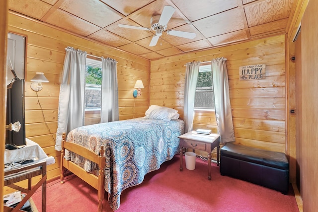 carpeted bedroom featuring wooden walls and a ceiling fan
