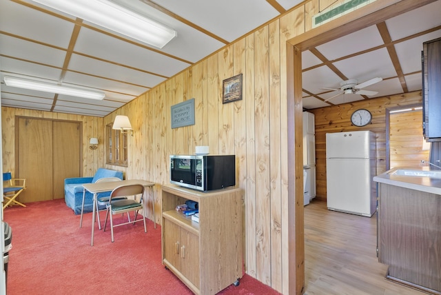 kitchen featuring freestanding refrigerator, stainless steel microwave, wood walls, a ceiling fan, and a sink