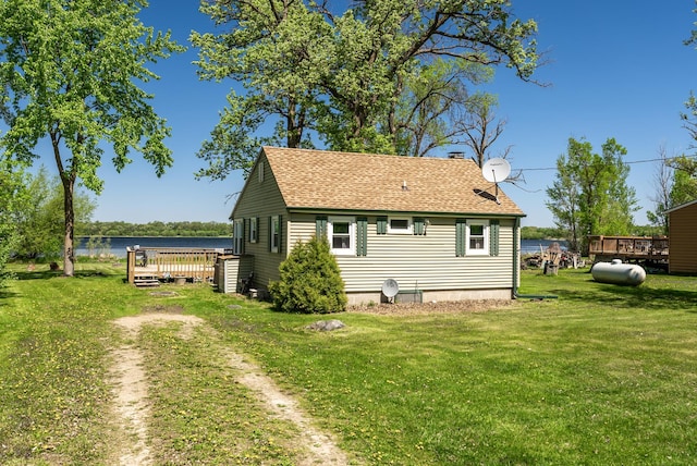 back of property with a deck with water view, roof with shingles, a yard, and a chimney