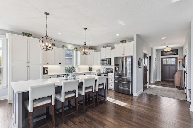 kitchen featuring white cabinets, appliances with stainless steel finishes, dark wood-type flooring, a center island, and light countertops