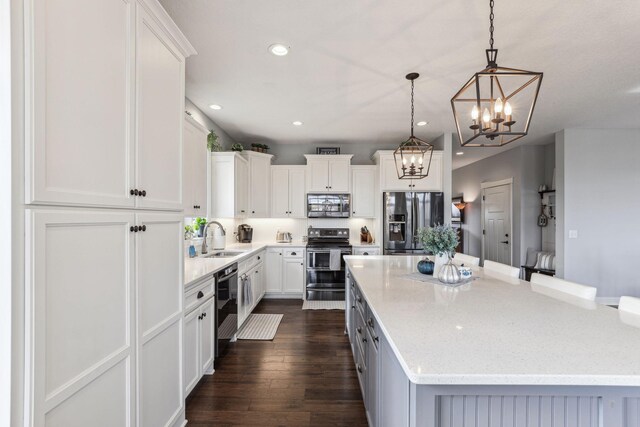 kitchen featuring stainless steel appliances, a sink, white cabinetry, a center island, and dark wood-style floors