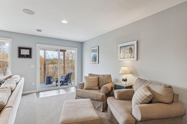 tiled living room with a textured ceiling, carpet floors, baseboards, and a healthy amount of sunlight