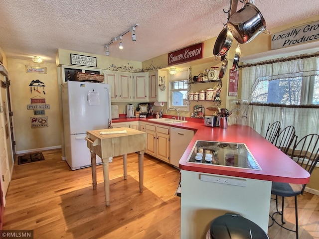 kitchen with white appliances, a breakfast bar area, a textured ceiling, light wood-style floors, and a sink