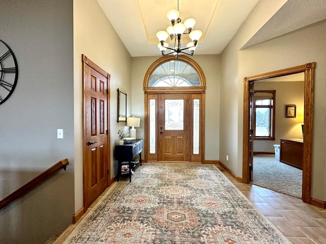 entryway with baseboards, stone finish floor, a raised ceiling, and an inviting chandelier