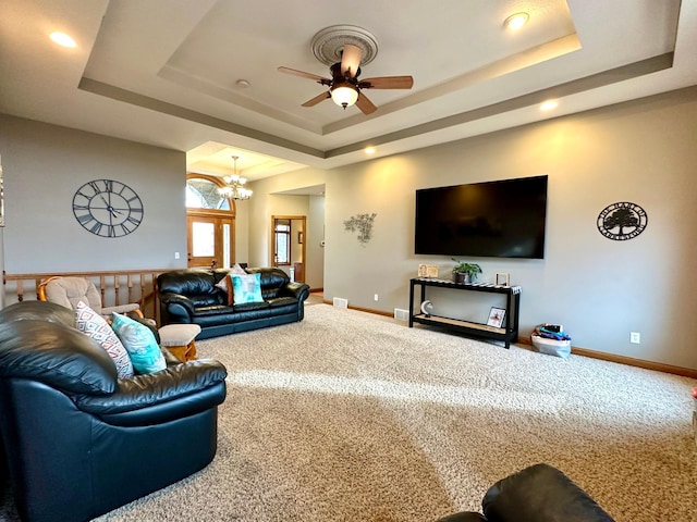 carpeted living room featuring baseboards, a tray ceiling, and ceiling fan with notable chandelier