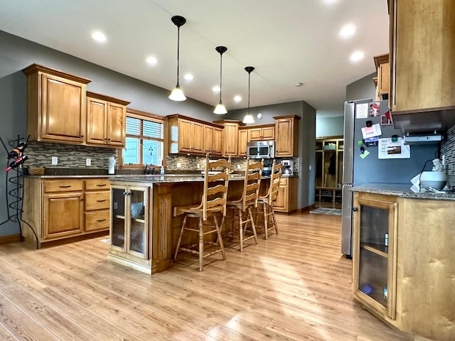 kitchen with brown cabinets, light wood-type flooring, stainless steel microwave, and a kitchen bar