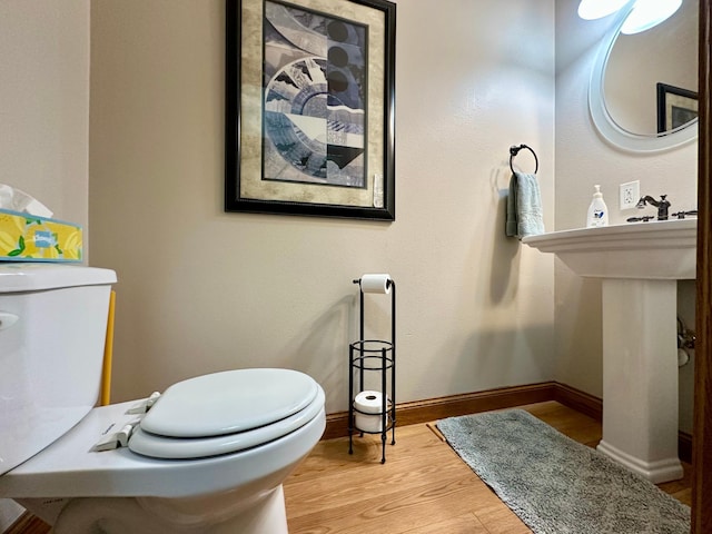 half bath featuring wood finished floors, toilet, and baseboards