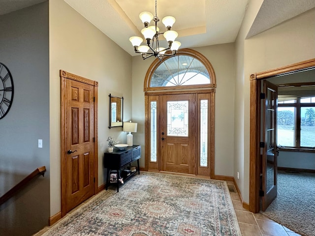 foyer with light tile patterned floors, light colored carpet, baseboards, a tray ceiling, and an inviting chandelier