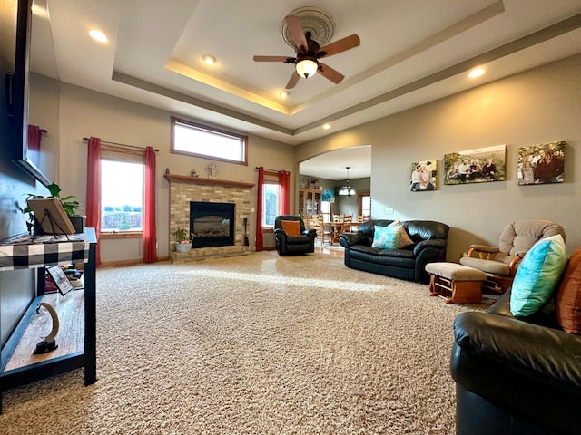 living area featuring arched walkways, ceiling fan, a brick fireplace, a tray ceiling, and carpet