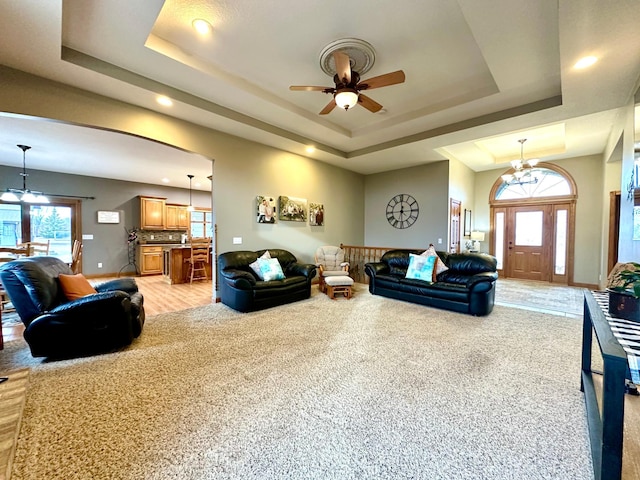 living room featuring a wealth of natural light, a raised ceiling, baseboards, and ceiling fan with notable chandelier